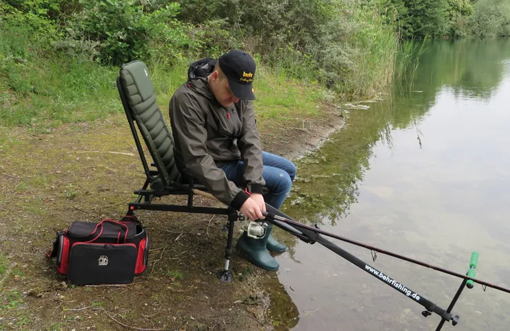 Angler sitzt in einem Stuhl am See und angelt.