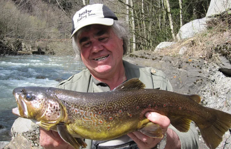 Angler hält einen Süßwasserfisch in den Händen und lächelt.